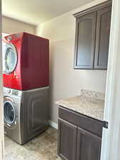 Laundry room featuring a textured ceiling, tile patterned flooring, cabinets, and stacked washer and dryer