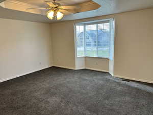 Unfurnished room featuring dark colored carpet, a textured ceiling, a tray ceiling, and ceiling fan