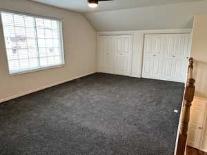 Unfurnished bedroom with multiple closets, lofted ceiling, and dark colored carpet