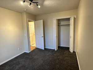 Unfurnished bedroom featuring a closet, dark carpet, and a textured ceiling