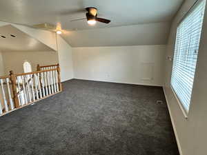 Additional living space with ceiling fan, plenty of natural light, dark carpet, and lofted ceiling