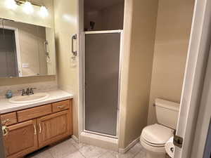 Bathroom featuring toilet, vanity, tile patterned floors, and a shower with door