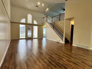 Unfurnished living room featuring ceiling fan, high vaulted ceiling, and dark wood-type flooring