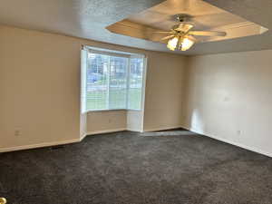 Carpeted empty room featuring a textured ceiling, a raised ceiling, and ceiling fan