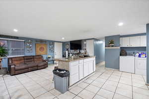 Kitchen featuring dark stone counters, separate washer and dryer, white cabinets, a kitchen island, and light tile patterned flooring