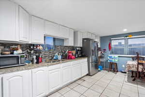 Kitchen featuring sink, tasteful backsplash, light tile patterned flooring, white cabinets, and appliances with stainless steel finishes