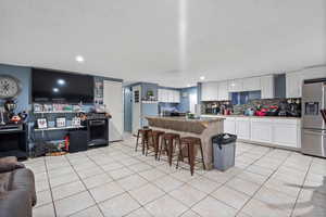 Kitchen featuring decorative backsplash, stainless steel fridge, a kitchen breakfast bar, white cabinetry, and a kitchen island