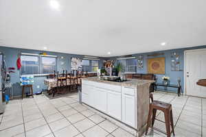 Kitchen featuring light tile patterned flooring, white cabinets, light stone countertops, black electric cooktop, and a kitchen island