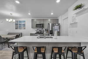 Kitchen with kitchen peninsula, appliances with stainless steel finishes, gray cabinetry, light hardwood / wood-style flooring, and a notable chandelier