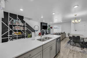 Kitchen featuring dishwasher, sink, light hardwood / wood-style flooring, a notable chandelier, and decorative light fixtures