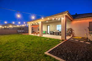 Back house at night featuring a yard and a patio