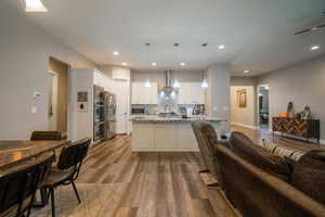 Kitchen with white cabinets, hanging light fixtures, light wood-type flooring, light stone countertops, and tasteful backsplash