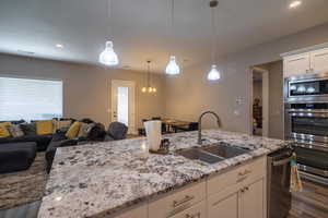 Kitchen with light stone countertops, white cabinetry, sink, and dark wood-type flooring