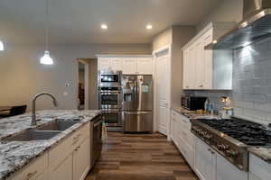 Kitchen featuring white cabinetry, sink, stainless steel appliances, and wall chimney range hood