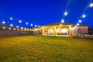 Back house at night featuring a yard and a patio area