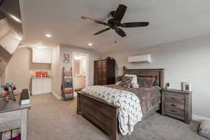 Carpeted bedroom featuring ceiling fan, lofted ceiling, an AC wall unit, and ensuite bath