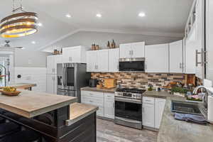 Kitchen featuring stainless steel appliances, light hardwood / wood-style flooring, white cabinets, hanging light fixtures, and lofted ceiling