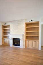 Unfurnished living room with a large fireplace, built in features, and light hardwood / wood-style flooring