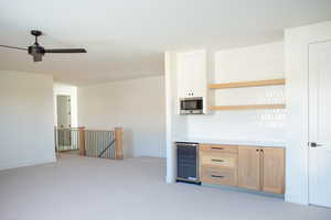 Interior space with stainless steel microwave, wine cooler, ceiling fan, and light brown cabinets