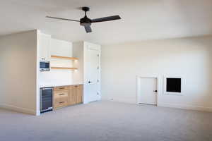 Unfurnished living room featuring light colored carpet, beverage cooler, and ceiling fan