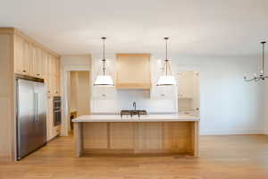 Kitchen featuring appliances with stainless steel finishes, light wood-type flooring, custom range hood, sink, and an island with sink