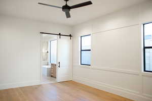 Unfurnished bedroom featuring connected bathroom, ceiling fan, light wood-type flooring, and a barn door