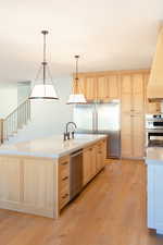 Kitchen with light brown cabinetry, appliances with stainless steel finishes, sink, light hardwood / wood-style floors, and hanging light fixtures