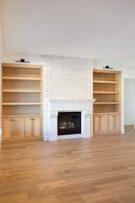 Unfurnished living room featuring built in shelves, a large fireplace, and light hardwood / wood-style floors