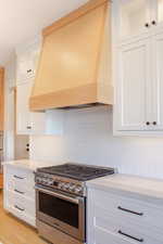 Kitchen with light hardwood / wood-style floors, white cabinetry, premium range hood, and stainless steel appliances