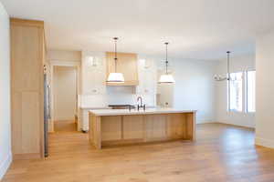 Kitchen with backsplash, a center island with sink, an inviting chandelier, light hardwood / wood-style flooring, and white cabinetry