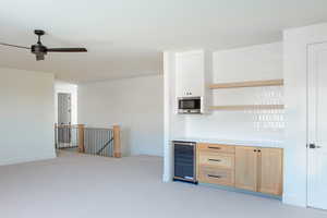 Kitchen with light brown cabinetry, stainless steel microwave, beverage cooler, and ceiling fan