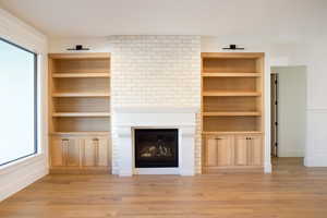 Unfurnished living room featuring a fireplace, built in shelves, and light wood-type flooring