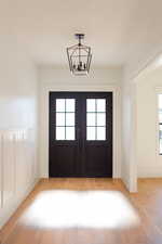 Doorway to outside featuring french doors, light hardwood / wood-style floors, and a notable chandelier