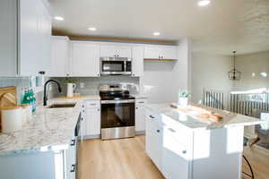 Kitchen with a center island, sink, hanging light fixtures, stainless steel appliances, and white cabinets