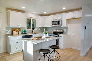 Kitchen with a center island, sink, appliances with stainless steel finishes, light hardwood / wood-style floors, and white cabinetry