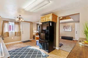 Kitchen with black fridge, a notable chandelier, a textured ceiling, light brown cabinetry, and light wood-type flooring