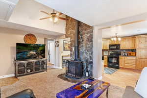 Living room with ceiling fan with notable chandelier, light wood-type flooring, and a wood stove