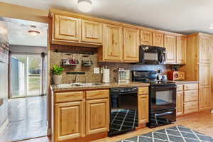 Kitchen featuring light brown cabinetry, a textured ceiling, sink, black appliances, and light hardwood / wood-style flooring