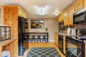 Kitchen featuring light brown cabinets, backsplash, black appliances, sink, and light hardwood / wood-style floors