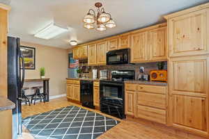 Kitchen with tasteful backsplash, light hardwood / wood-style flooring, a chandelier, light brown cabinetry, and black appliances