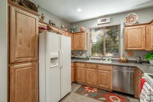 Kitchen featuring light tile patterned floors, appliances, and sink with window looking into front yard.