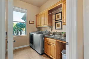 Laundry area with separate washer and dryer, sink, light tile patterned floors, and cabinets