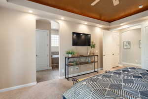 Bedroom featuring ceiling fan, light carpet, and ensuite bath