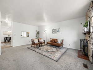 Living room featuring carpet flooring, a notable chandelier, a wood stove, and a textured ceiling