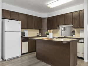 Kitchen featuring decorative backsplash, a textured ceiling, dark brown cabinetry, light hardwood / wood-style flooring, and white fridge