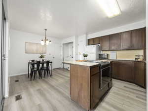 Kitchen featuring range, white refrigerator, light hardwood / wood-style floors, and hanging light fixtures