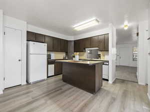 Kitchen with a textured ceiling, white refrigerator, light hardwood / wood-style floors, and dark brown cabinetry