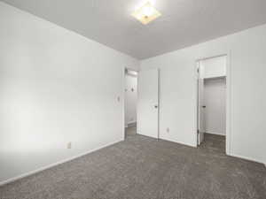 Unfurnished bedroom featuring a walk in closet, a closet, and dark colored carpet