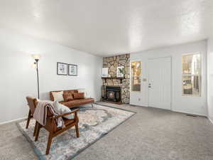 Carpeted living room with a textured ceiling, a wood stove, and plenty of natural light