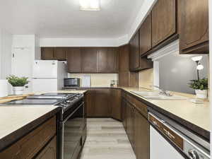 Kitchen featuring a textured ceiling, dark brown cabinetry, sink, black appliances, and light hardwood / wood-style flooring